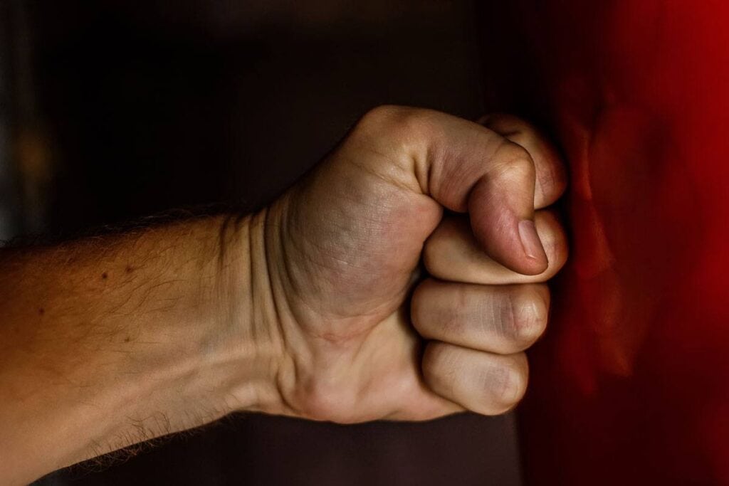 A close-up of a clenched fist striking a red punching bag, showing the impact and slight indentation on the bag.
