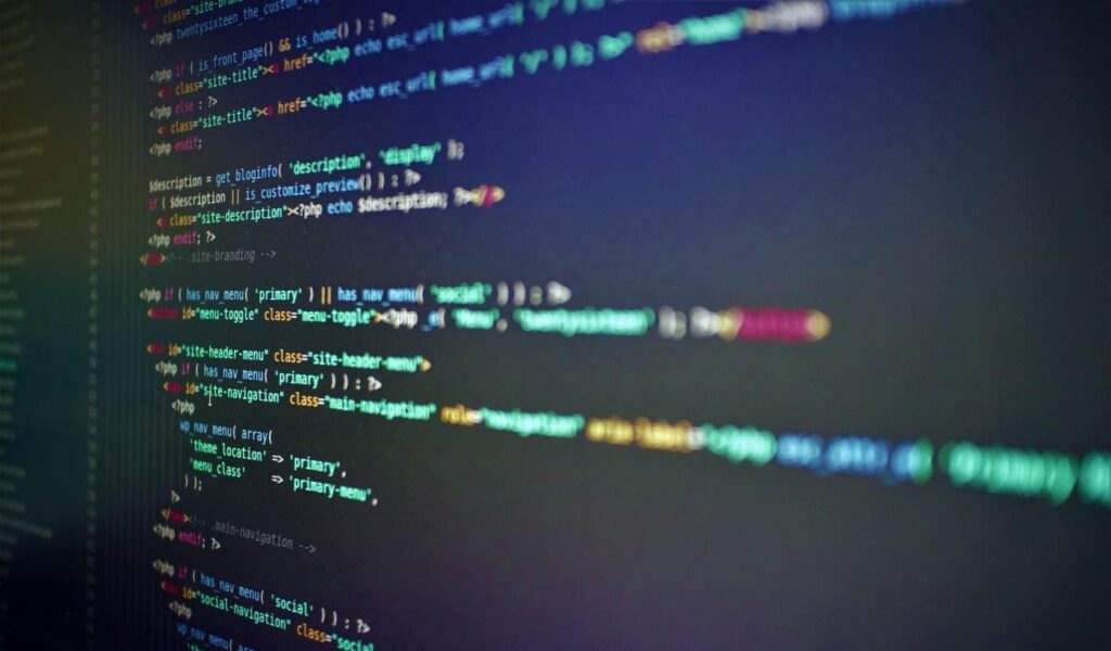 Close-up of a computer screen displaying colorful lines of HTML and PHP code on a dark background, indicating web development or programming work in progress.