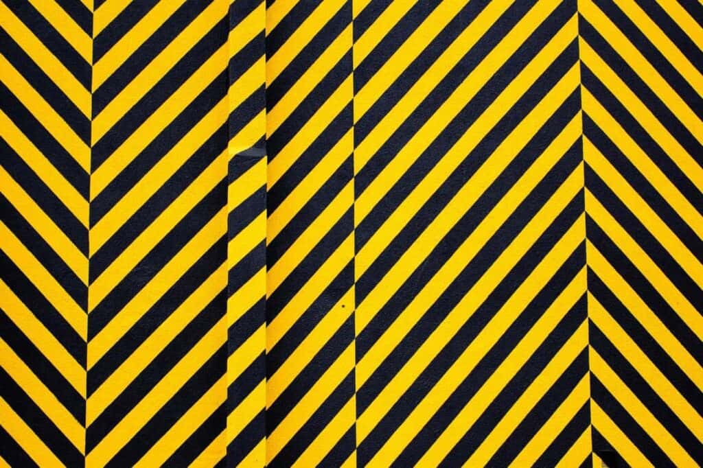 Black and yellow diagonal stripes create a bold, repetitive pattern, resembling caution tape. The lines are parallel, with a slight vertical break near the center, adding visual interest to the geometric design.