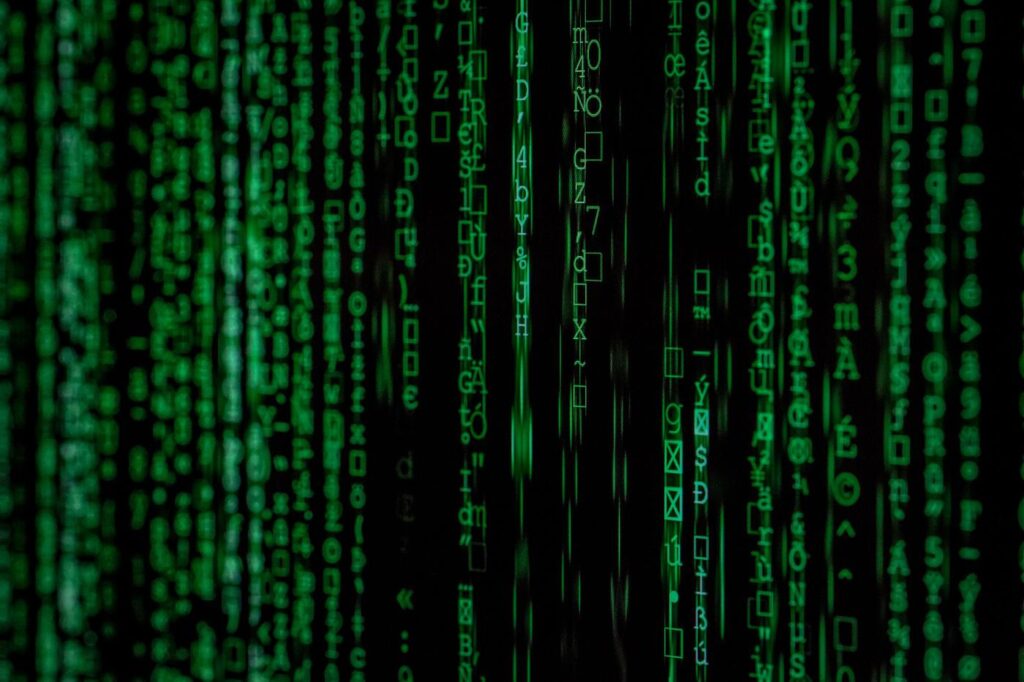 Green code symbols cascade vertically on a black background, resembling the digital rain effect from the Matrix movie series. The characters include numbers, letters, and various symbols in different sizes and brightness.