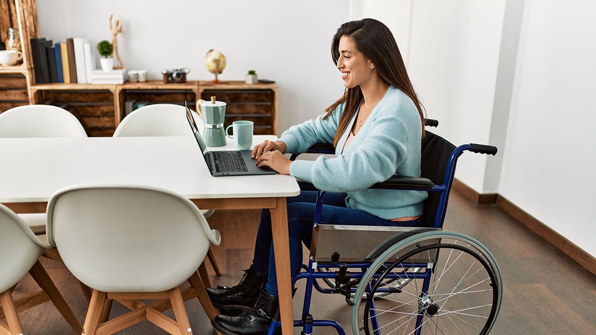 Adult Woman in Wheelchair Working on Laptop at the End of a Table
