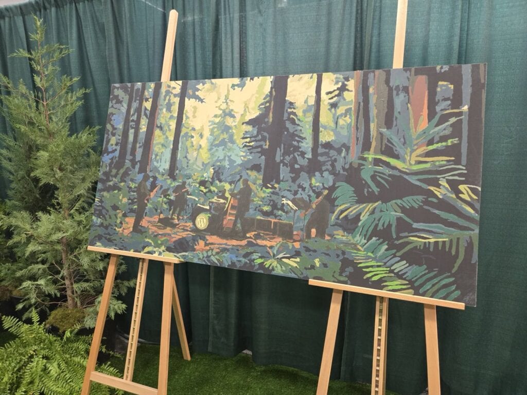 Wordcamp'S Community Painting Rests On Two Easels. The Canvas Depicts A Forest Scene With Tall Trees And Dense Foliage, Surrounded By Actual Potted Plants. A Green Curtain Hangs In The Background.
