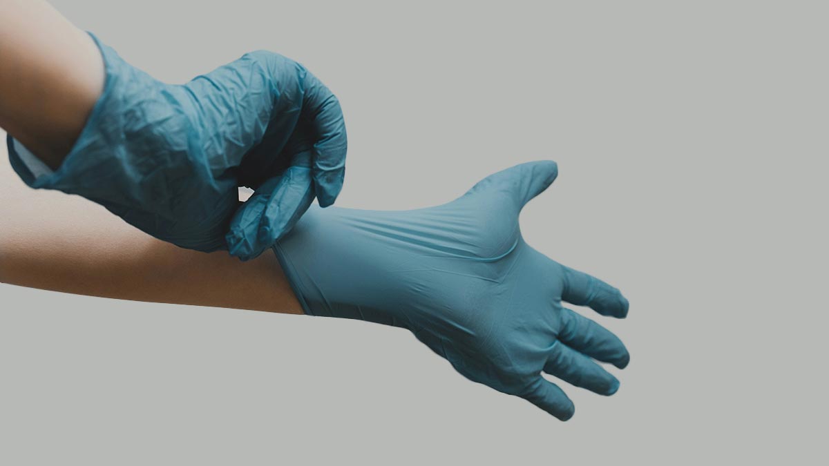 A person wearing blue disposable gloves, adjusting one on their left hand. The background is a plain light gray.