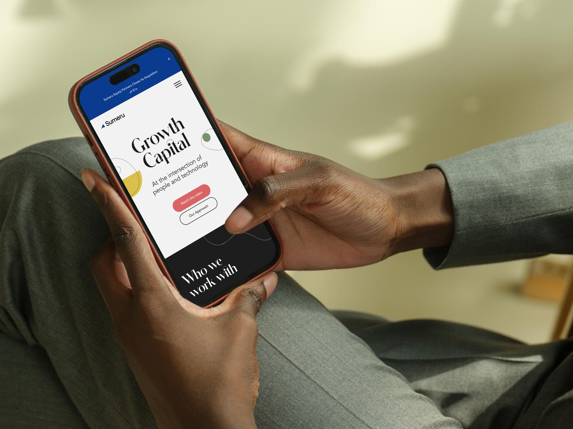 A Person In A Suit Holds A Smartphone, Browsing A Website About Growth Capital. The Phone Screen Displays A Site With A “Get Started” Button And Information About People And Relationships.