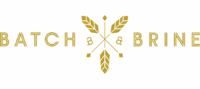Logo For Batch &Amp; Brine Featuring Golden Text With Two Crossed Wheat Stalks And Arrows In The Center, Stylized Ampersands Between The Words. White Background.