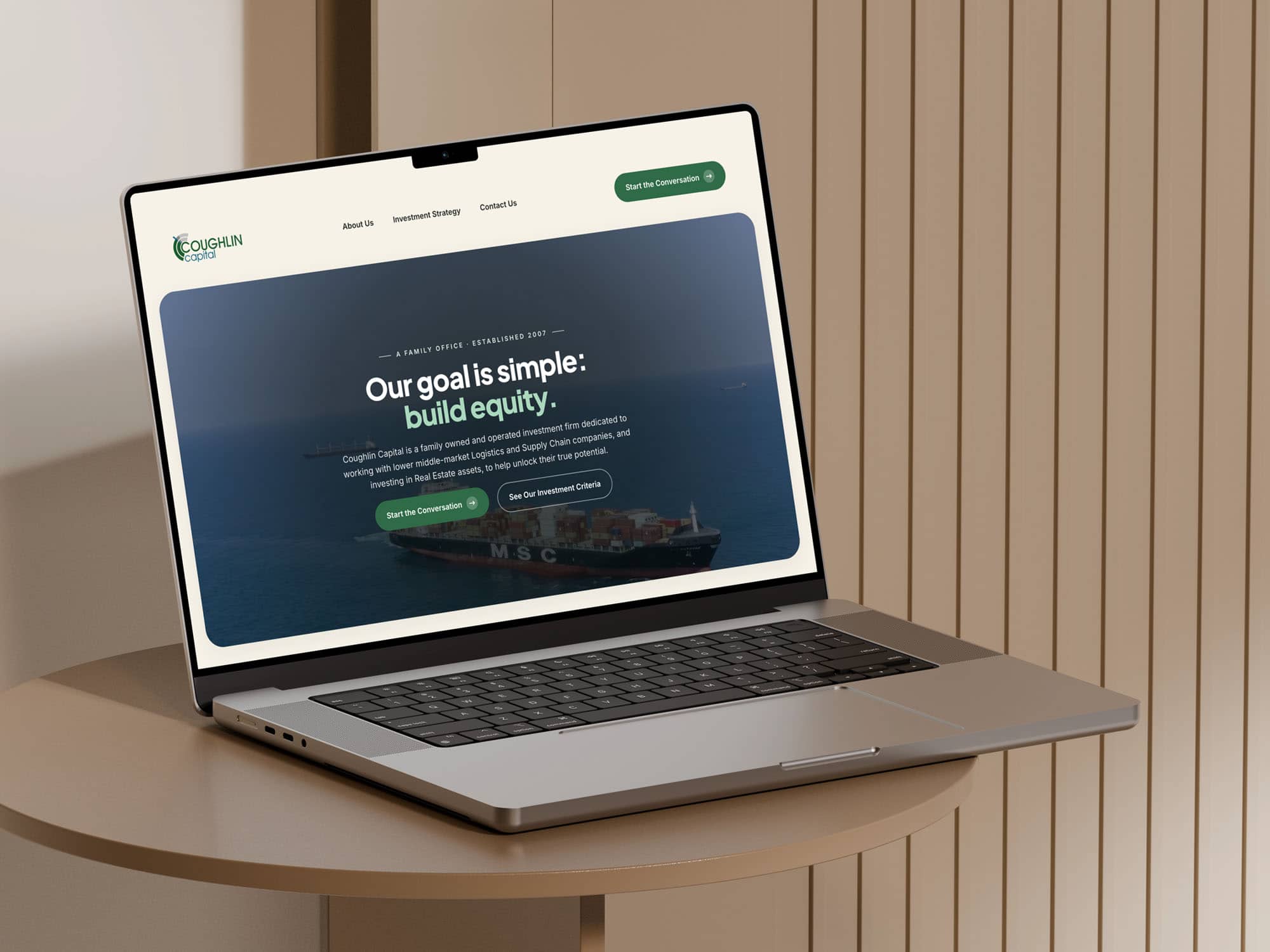 A Laptop On A Beige Table Displays A Website Homepage With The Headline “Our Goal Is Simple: Build Equity” Over An Image Of A Cargo Ship.